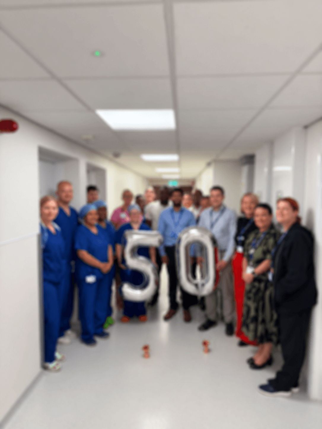 Healthcare workers in a hospital hallway celebrating a 50th anniversary with large silver balloons.