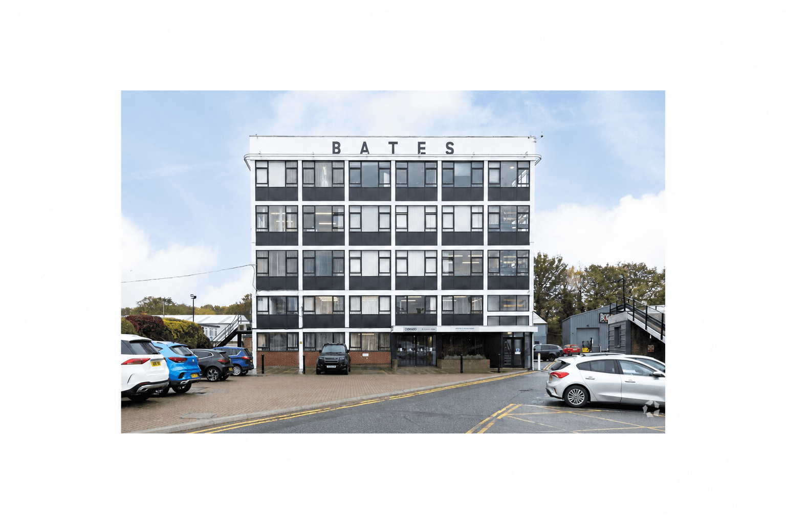Five-story white office building with BATES sign and black windows overlooking a parking lot.