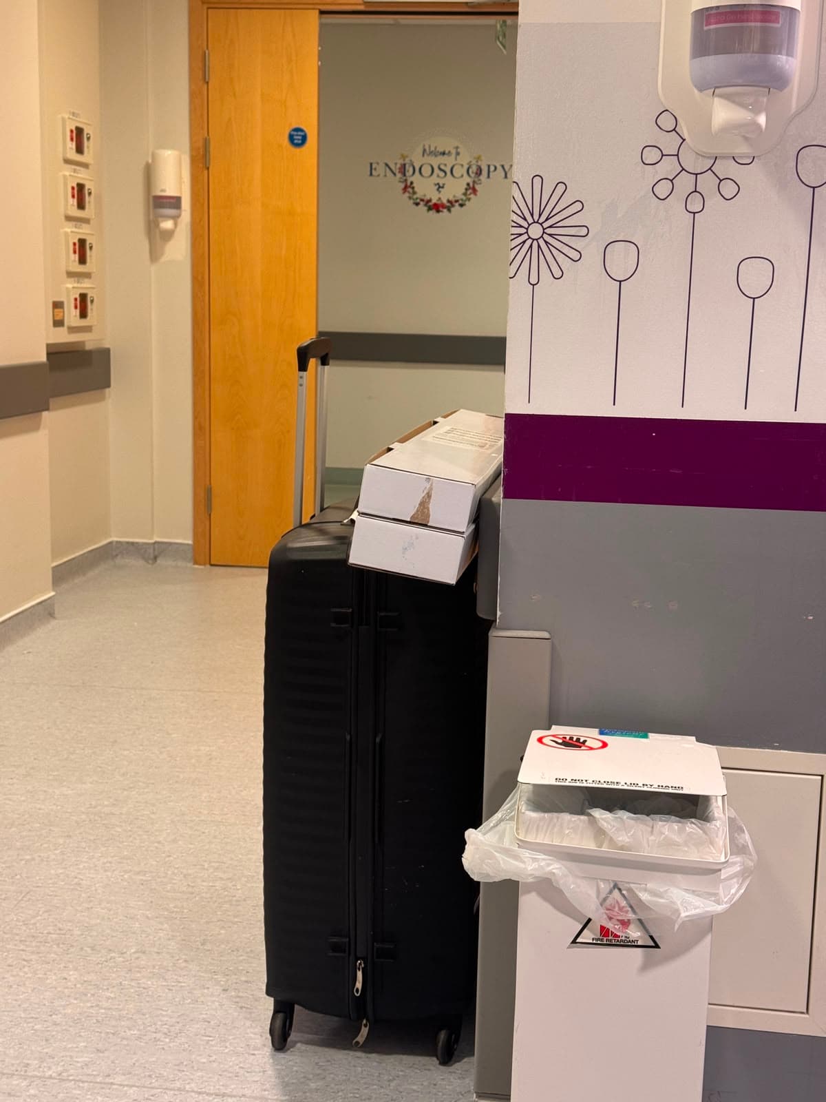 Black suitcase with white boxes in a hospital corridor near a 'Welcome to Endoscopy' sign.